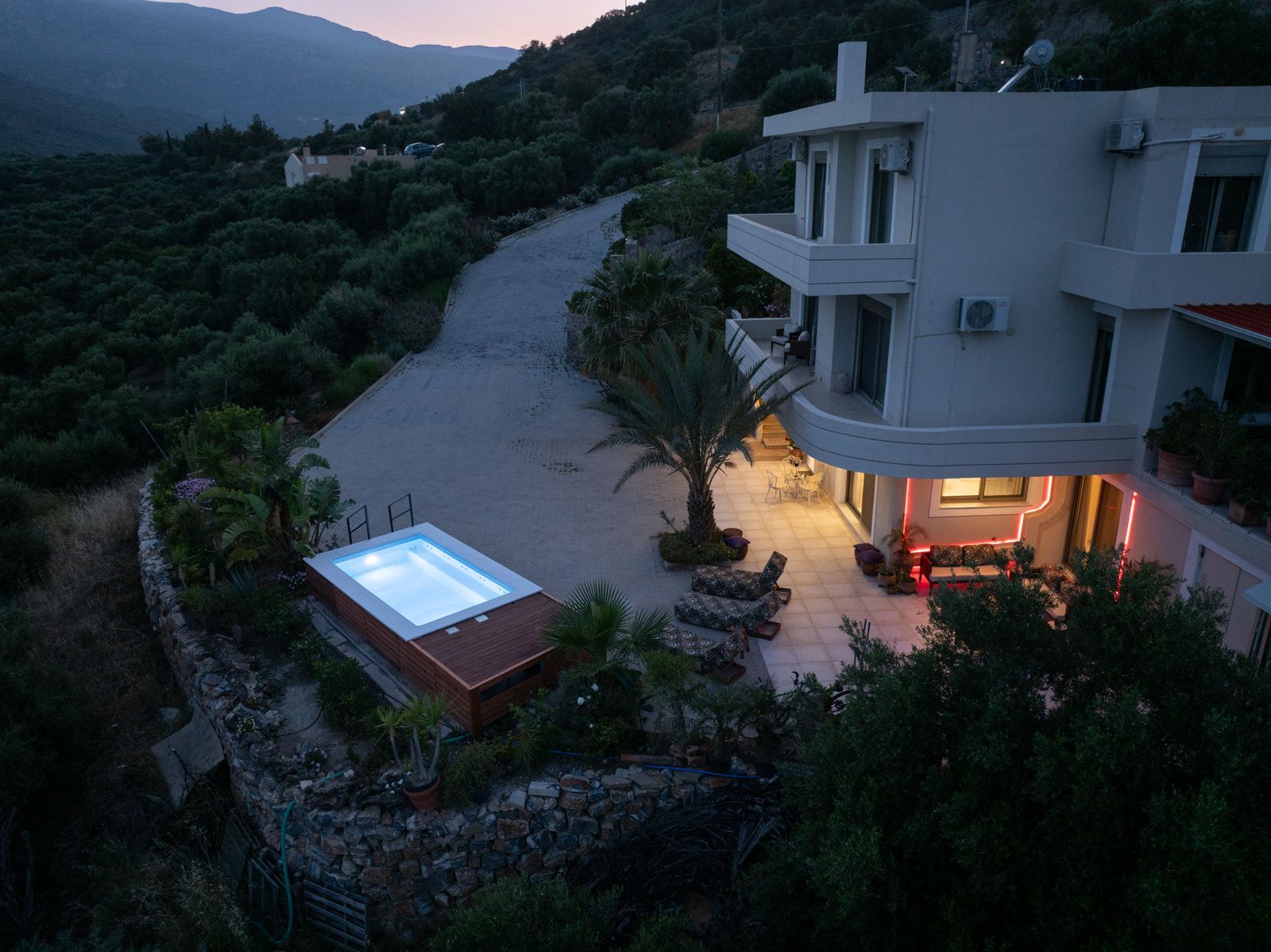The house glowing at dusk above the lit pool, hills all around