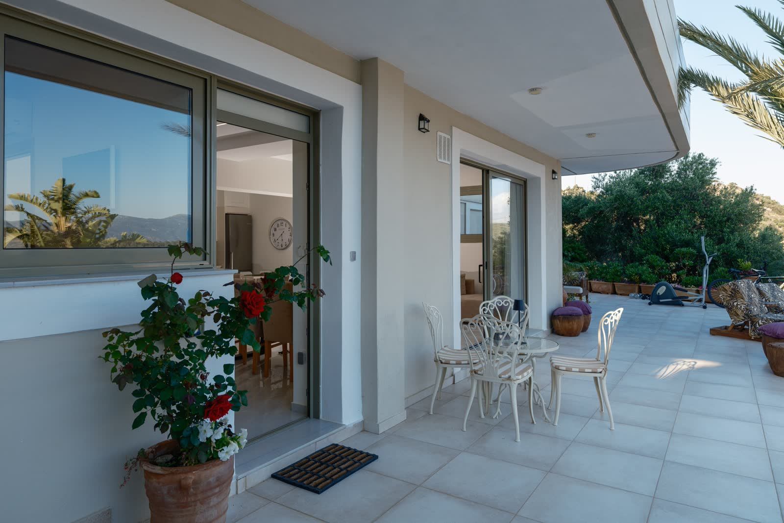 The entrance — white chairs, a pot of red roses and the open door