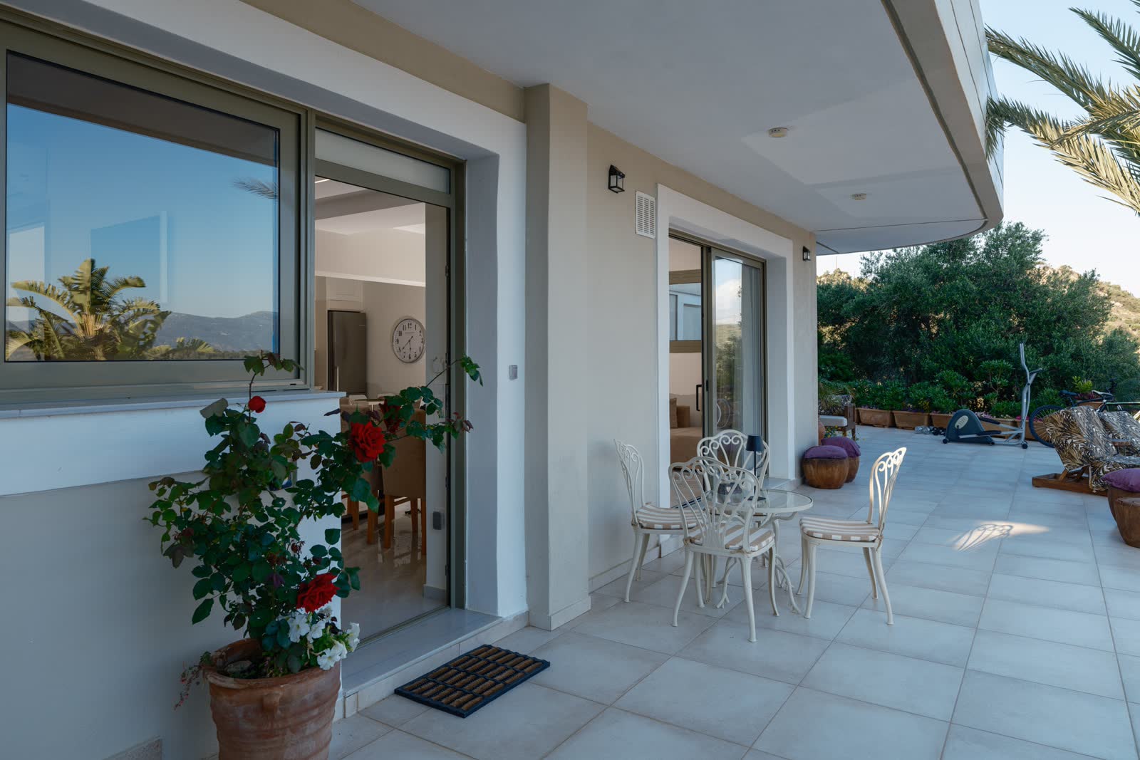 The entrance — white chairs, a pot of red roses and the open door